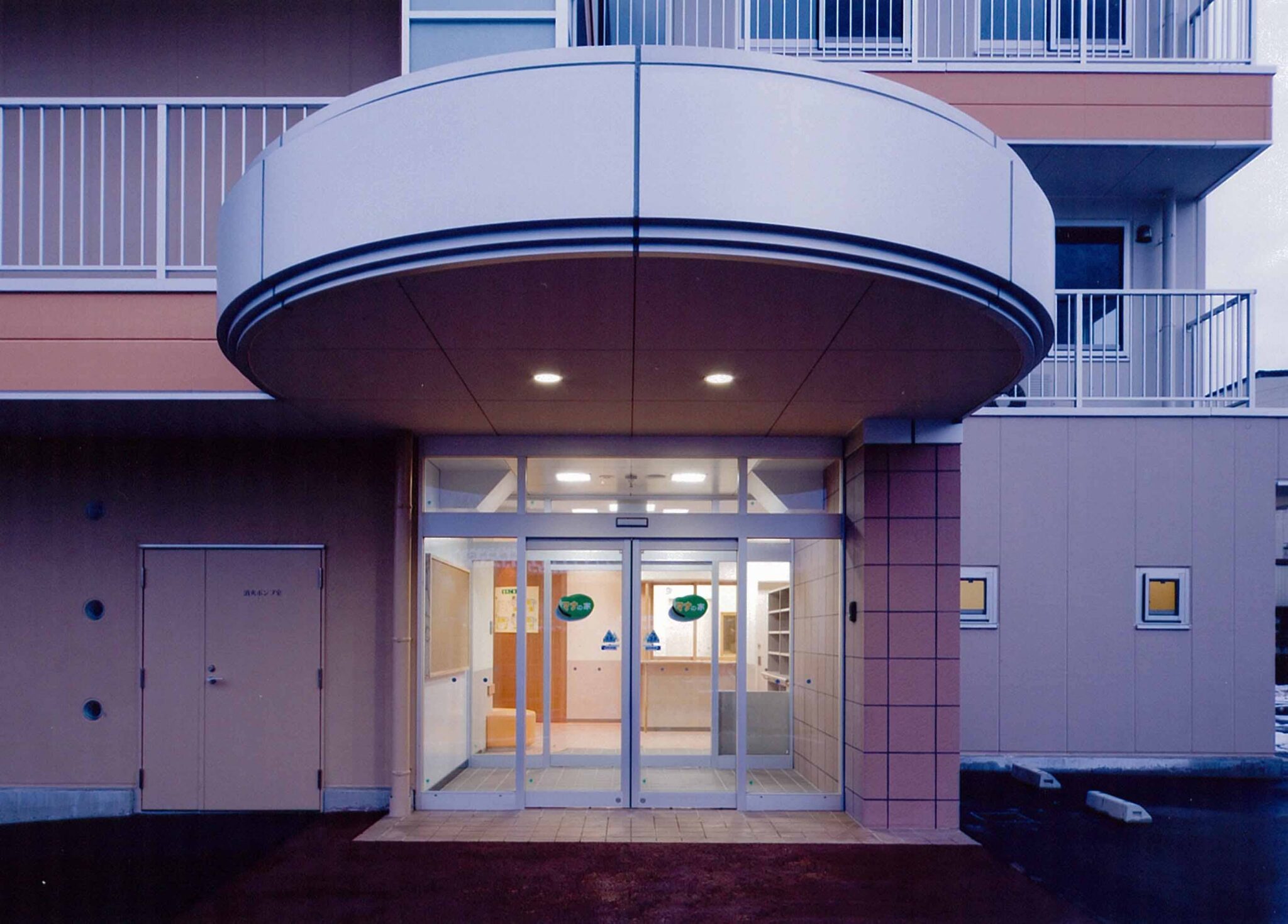 モダンな曲線デザインの玄関・エントランス。夜間撮影で建物外観も見える